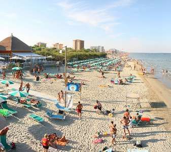 Spiaggia affollata con persone, ombrelloni e mare calmo sotto un cielo sereno.