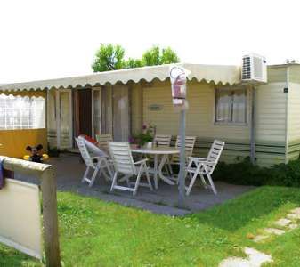 Casa mobile con tavolo e sedie bianche all'aperto sotto una tenda.