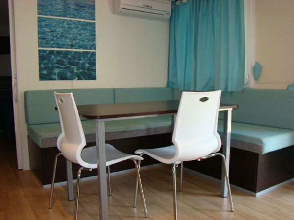 Una sala da pranzo con tavolo, due sedie bianche, divano angolare e tende azzurre.