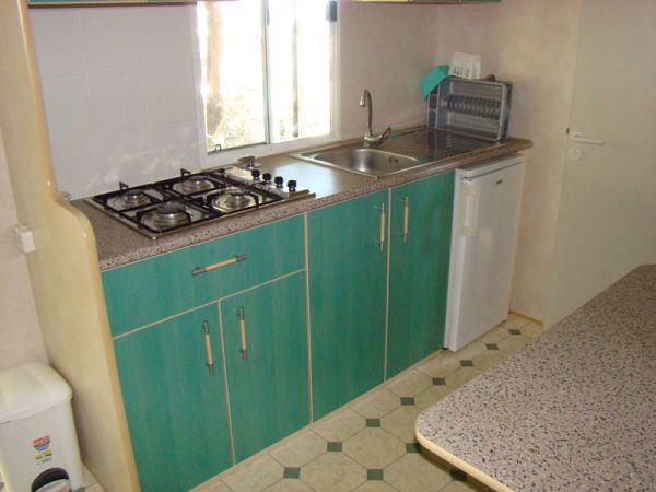 Cucina con mobili blu, lavandino, fornelli a gas e mini frigo.