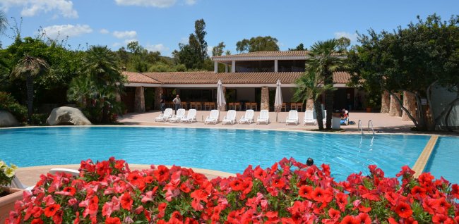 Piscina con fiori rossi e lettini bianchi.