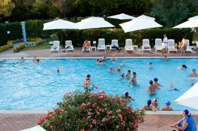 Piscina affollata con ombrelloni bianchi e rigogliosi cespugli fioriti.