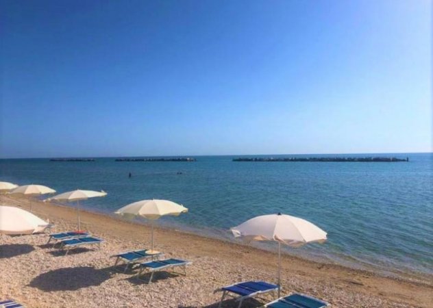 Spiaggia di ghiaia con ombrelloni e mare calmo.