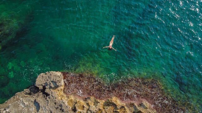 Persona che nuota nel mare vicino a scogli.