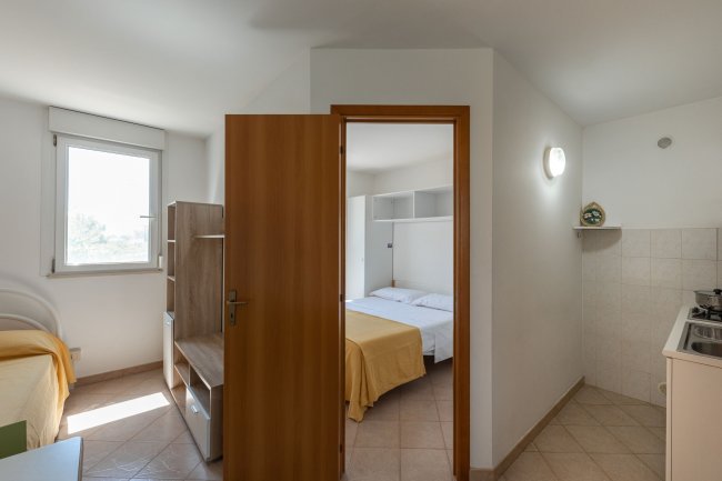 Entrata verso camera da letto e cucina, letto matrimoniale visibile.