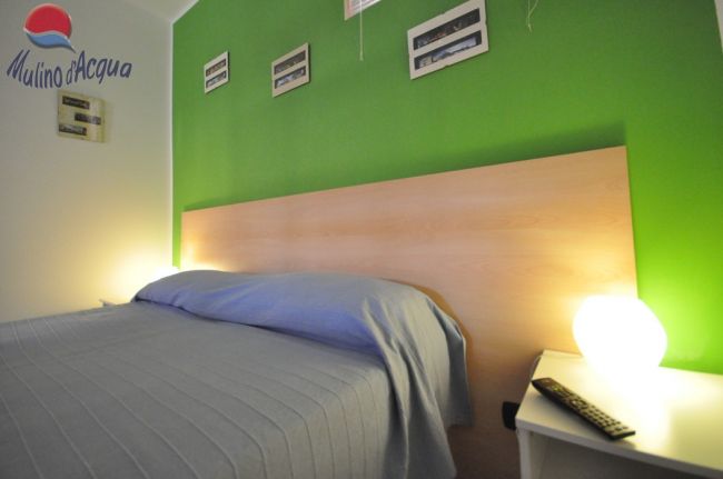 Camera con parete verde, letto matrimoniale e illuminazione soffusa.