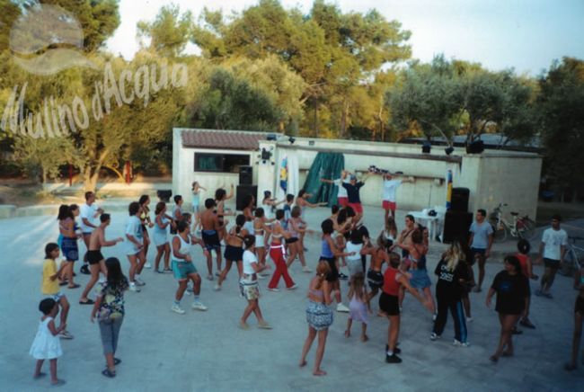 Gruppo di persone che ballano all'aperto su una piattaforma circondata da alberi.