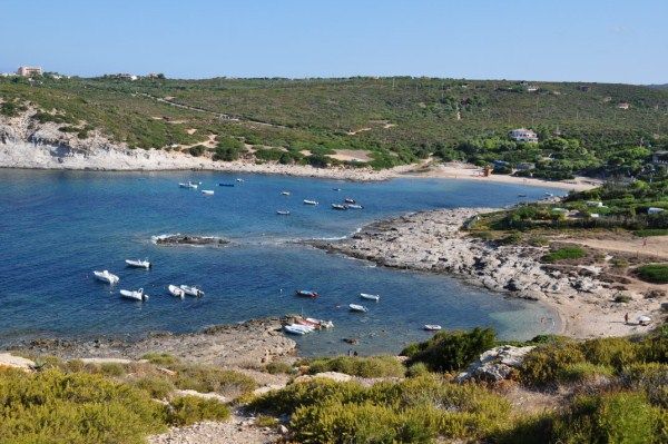 Baia con piccole barche ancorate vicino a una costa rocciosa e colline verdi.