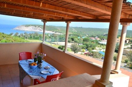 Terrazza coperta con tavolo apparecchiato, vista su mare e colline.
