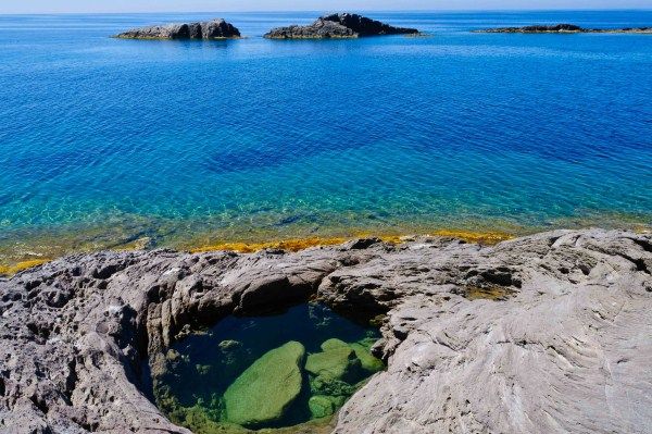 Laghetto roccioso vicino a un mare azzurro con isole in lontananza.