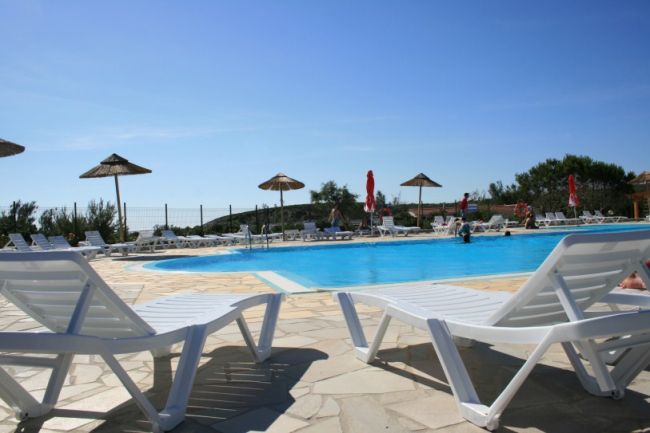 Piscina circondata da lettini e ombrelloni sotto il sole.