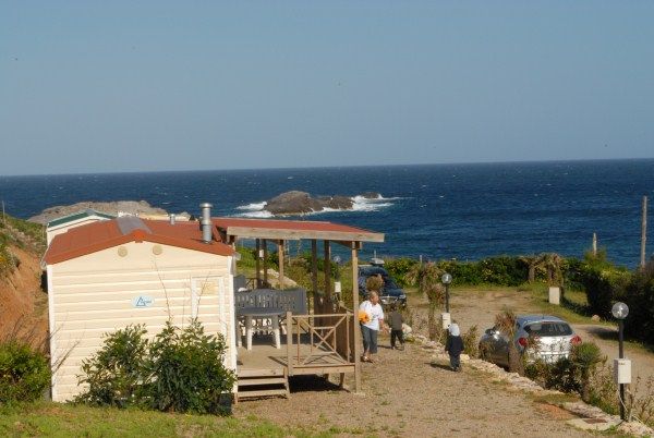 Casa mobile vicino al mare con persone sul vialetto. Cielo sereno e spiaggia in lontananza.