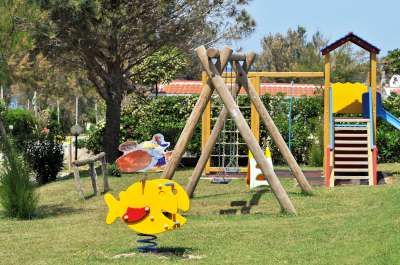 Parco giochi con altalene e giochi a molla, su un prato verde.