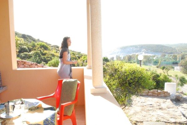 Una persona guarda il paesaggio da una veranda soleggiata, con tavolo e sedia.