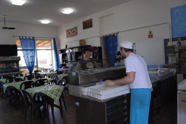 Interno di un ristorante con tavoli apparecchiati e cuoco al lavoro.