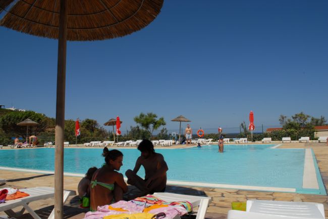 Piscina con persone sedute sotto un ombrellone.