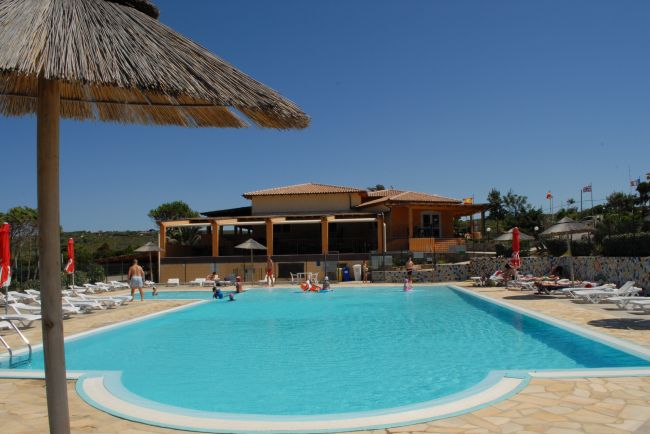 Piscina esterna con ombrellone e edificio sullo sfondo.