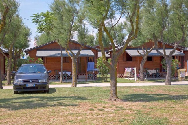 Bungalow di legno tra gli alberi, auto parcheggiata davanti.
