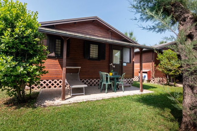 Bungalow in legno con veranda e sedie verdi.