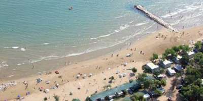 Spiaggia sabbiosa con ombrelloni, bagnanti e un molo di pietre.