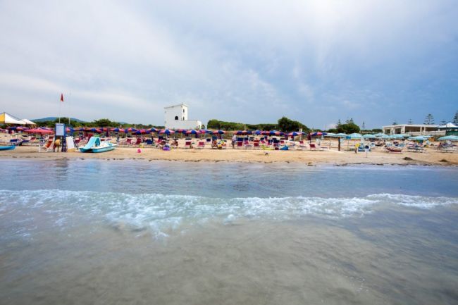 Spiaggia vista dal mare con ombrelloni e torre sullo sfondo.