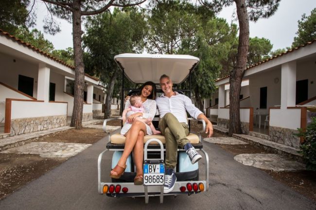 Famiglia su un golf cart tra villette bianche e alberi.