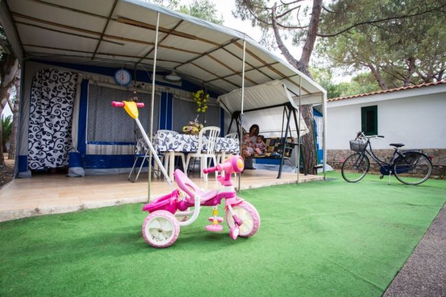 Tenda con triciclo rosa davanti; bici accanto all'ingresso.