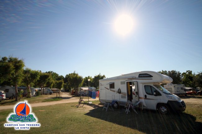 Un camper parcheggiato su un prato sotto il sole splendente.