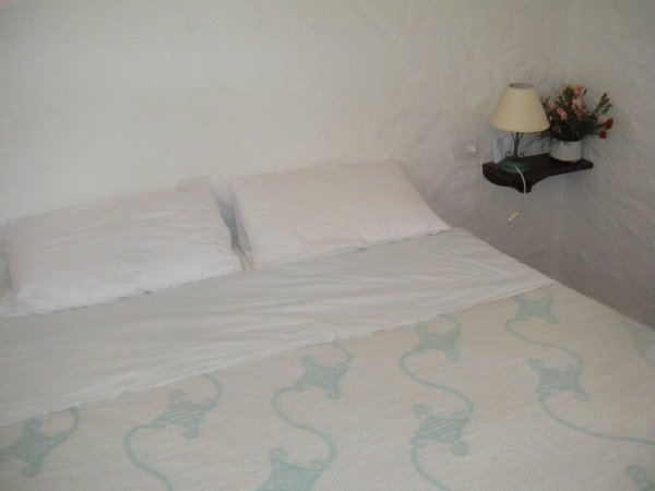 Letto matrimoniale con lampada e fiori su ripiano.