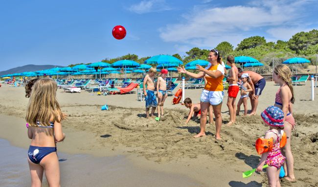 Persone giocano a palla su una spiaggia con ombrelloni blu.