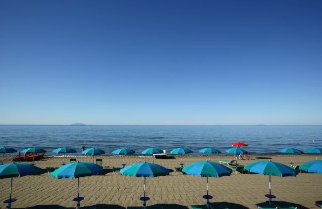 Spiaggia sabbiosa con ombrelloni blu e mare calmo.