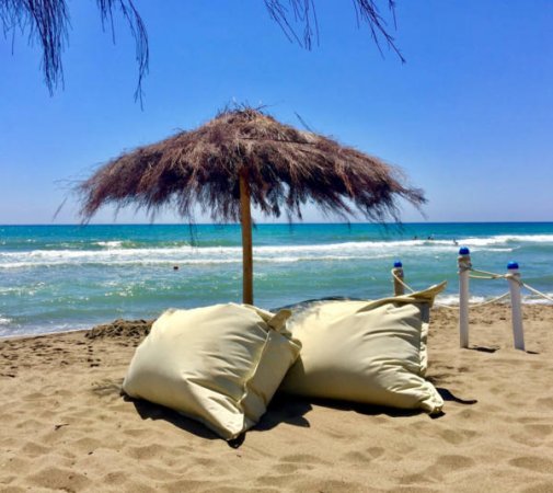 Spiaggia con ombrellone di paglia e cuscini.