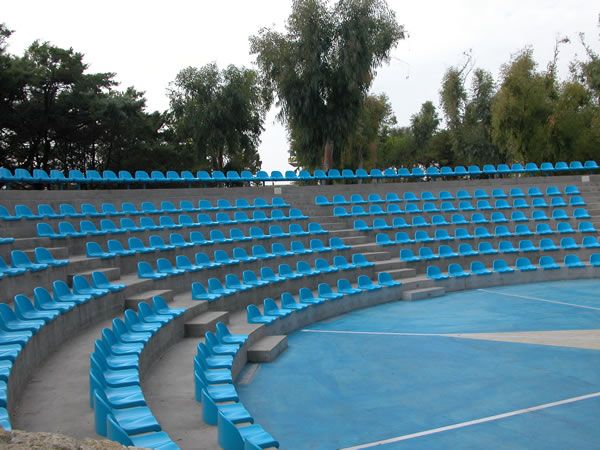 Anfiteatro all'aperto con file di sedili blu e alberi sullo sfondo.