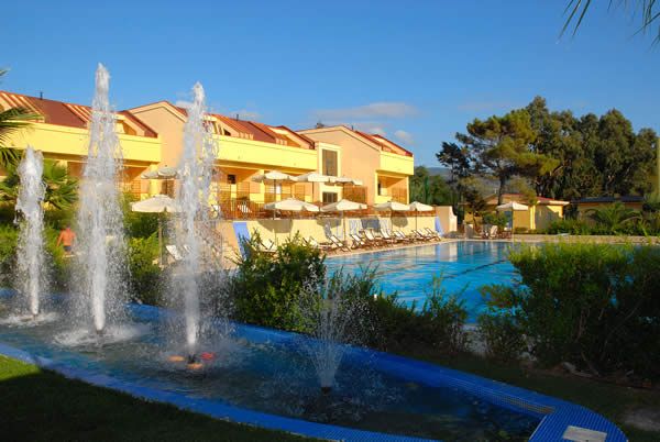 Una struttura con una piscina, circondata da lettini e ombrelloni, e una fontana in primo piano.