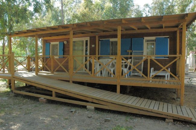 Veranda in legno con rampa d'accesso e sedie bianche sul patio.