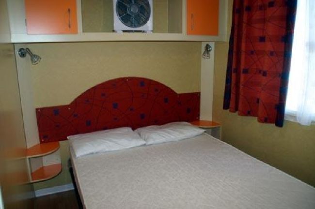 Camera con letto matrimoniale, testiera rossa decorata e armadi arancioni.