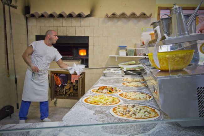Un uomo che prepara pizze davanti a un forno in una pizzeria.