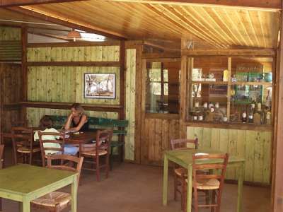 Tavoli e sedie di legno in un interno rustico con una persona seduta in un angolo.
