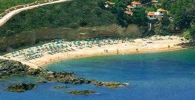 Veduta aerea di una spiaggia affollata con ombrelloni e un mare blu profondo.