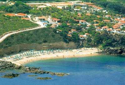 Una spiaggia con ombrelloni vicino a una scogliera e case sulla collina.
