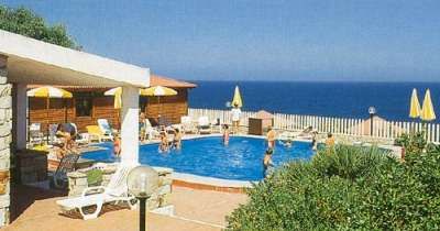 Piscina esterna con bambini che nuotano, vista sul mare e ombrelloni gialli.