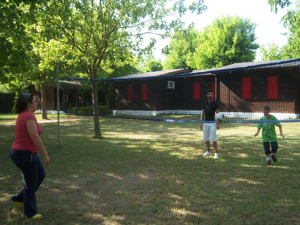 Due persone giocano a pallavolo in giardino con una palla. Alberi e un edificio sullo sfondo.