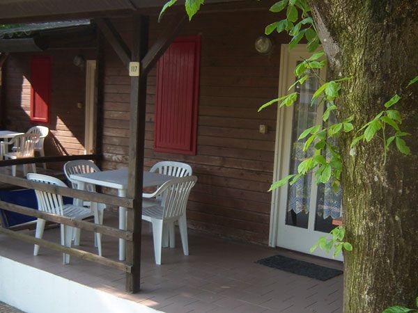 Una veranda in legno con tavolo e sedie bianche sotto un albero.