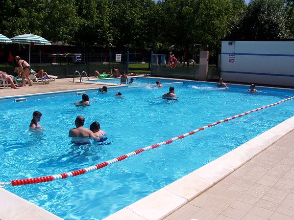 Piscina esterna con persone che nuotano e si rilassano al sole.