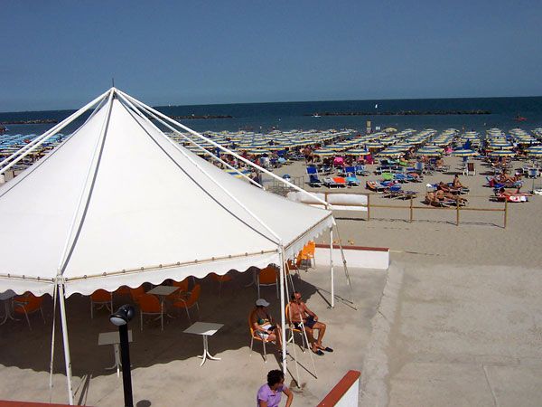 Una spiaggia affollata con lettini e un grande gazebo bianco vicino al mare.