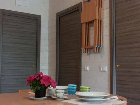 Tavolo apparecchiato con fiori, piatti e tazze, porte sullo sfondo.