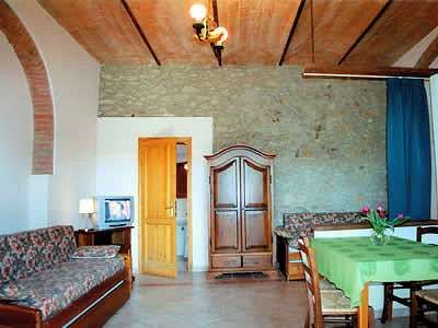 Soggiorno con divano fiorito, armadio in legno, tavolo con tovaglia verde, e parete in pietra.