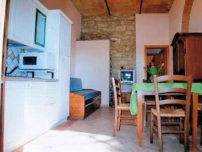 Cucina con mobili bianchi e microonde, tavolo con tovaglia verde e sedie, piccolo divano.