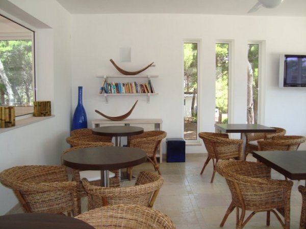 Sala con tavoli, sedie intrecciate e libreria.