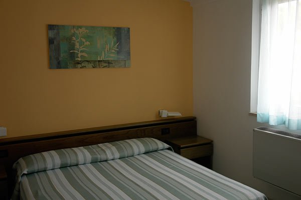 Una camera con un letto matrimoniale, parete gialla e quadro floreale.